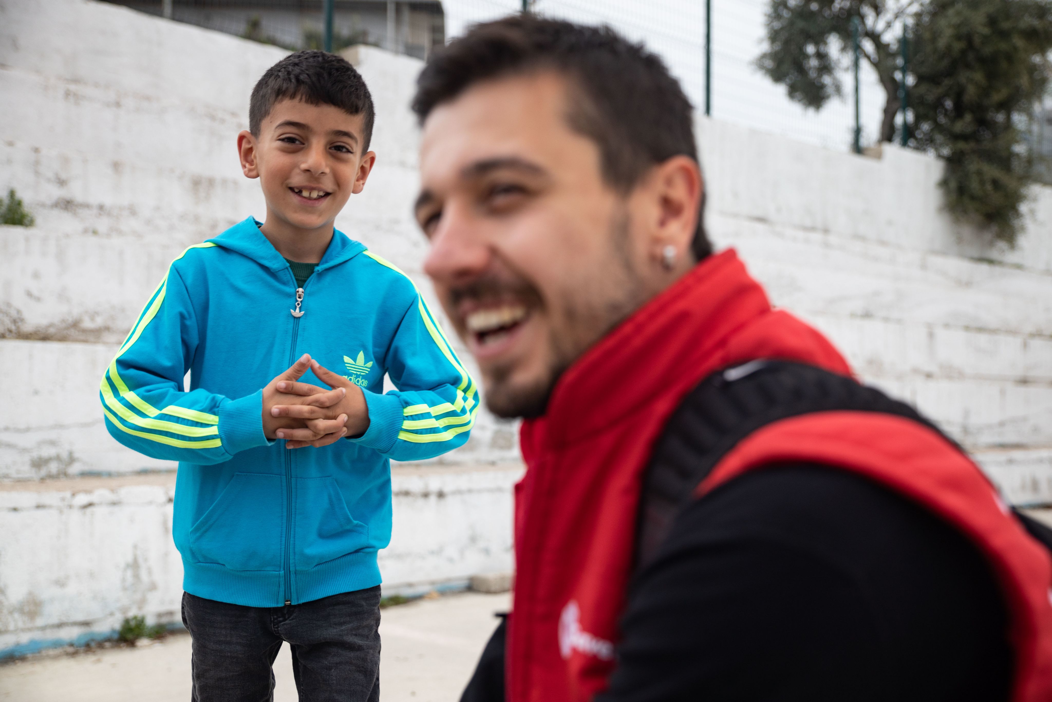 A boy smiling at the camera standing next to a Save the Children staff person.
